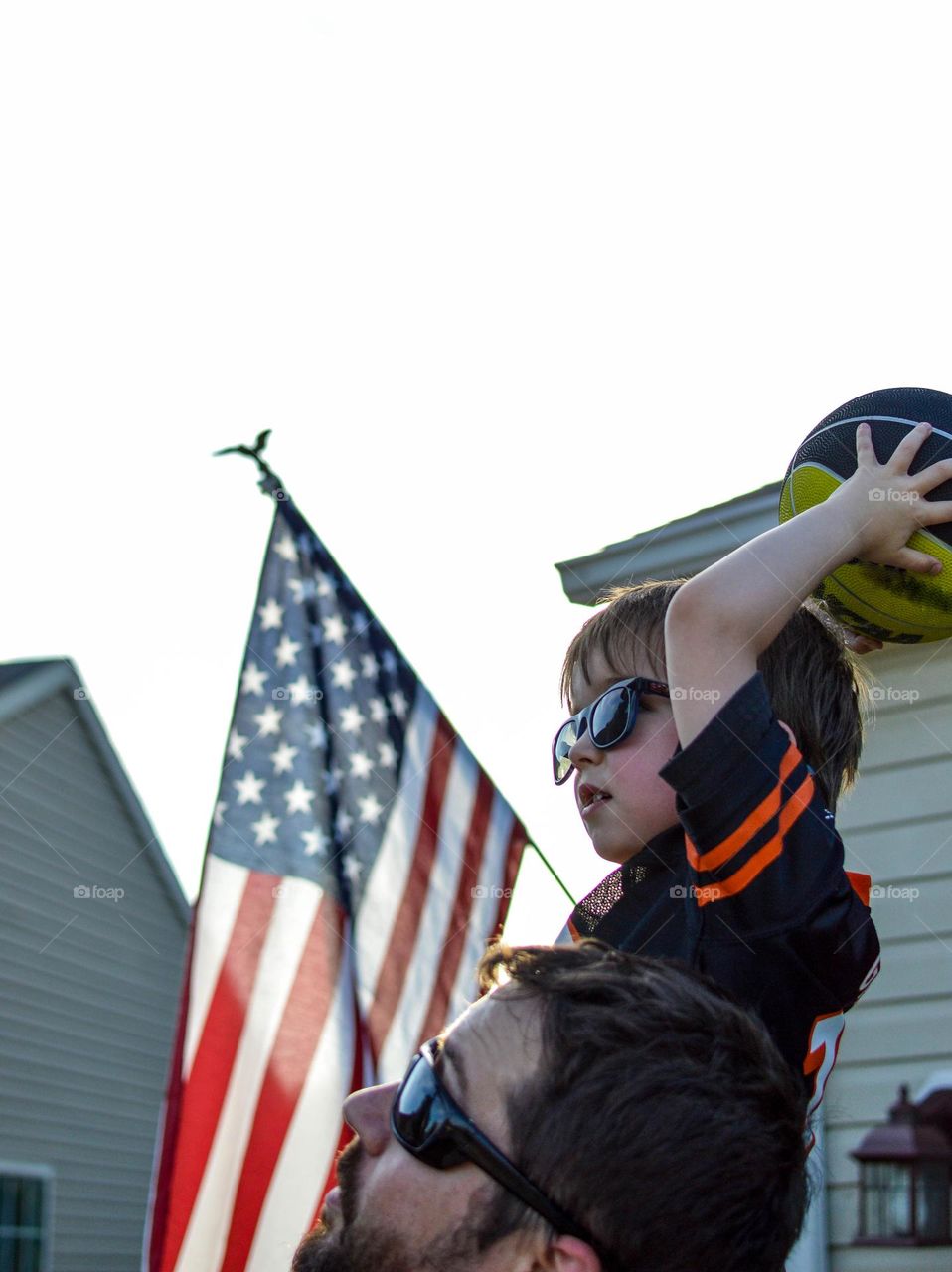 Toddler boy throwing a basketball while sitting on his father’s shoulder 
