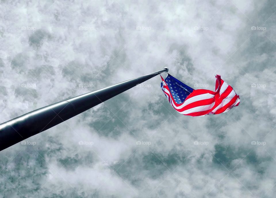A tall American flag above reaching up to the sky- cloudy sky