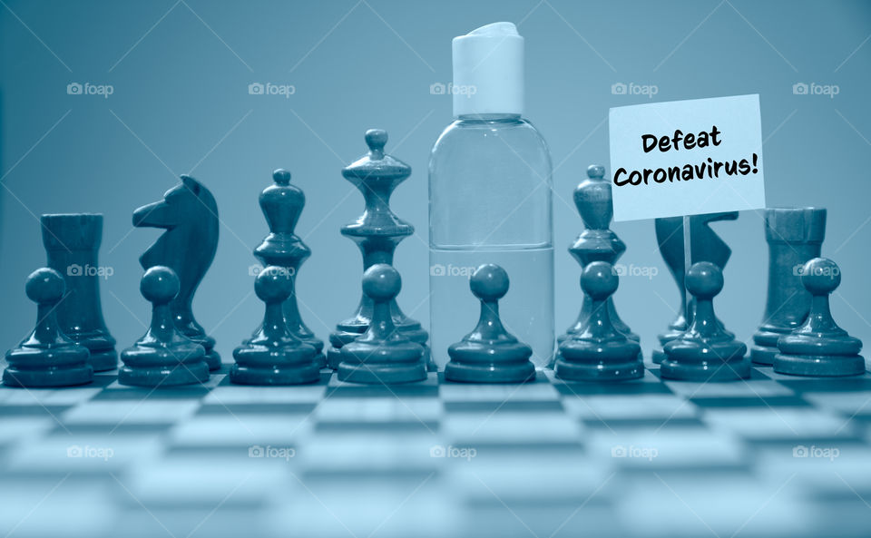 Coronavirus concept image chess pieces and hand sanitizer on chessboard illustrating global struggle against novel covid-19 outbreak with defeat coronavirus sign.