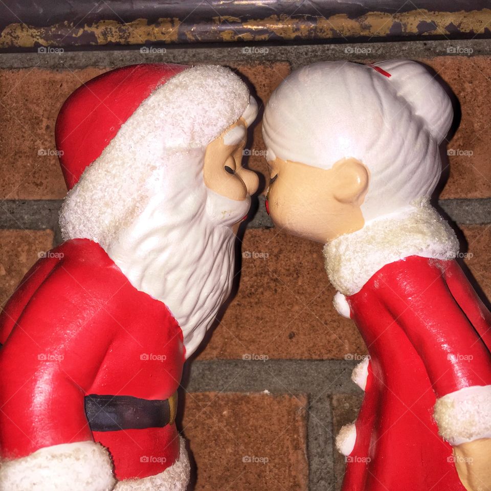 Ceramic figurines of Santa and Mrs. Claud kissing in front of a brick wall. These classic figures are older and collectible.