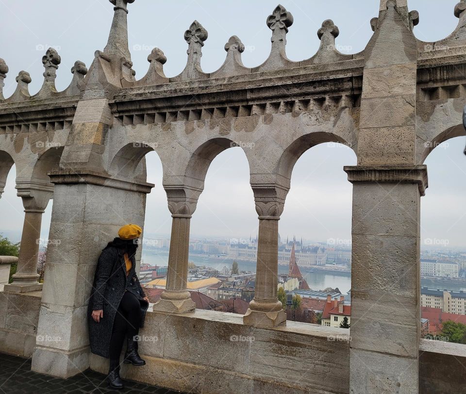 girl with yellow hat looking through architectural window wall frame towards Budapest, Hungary