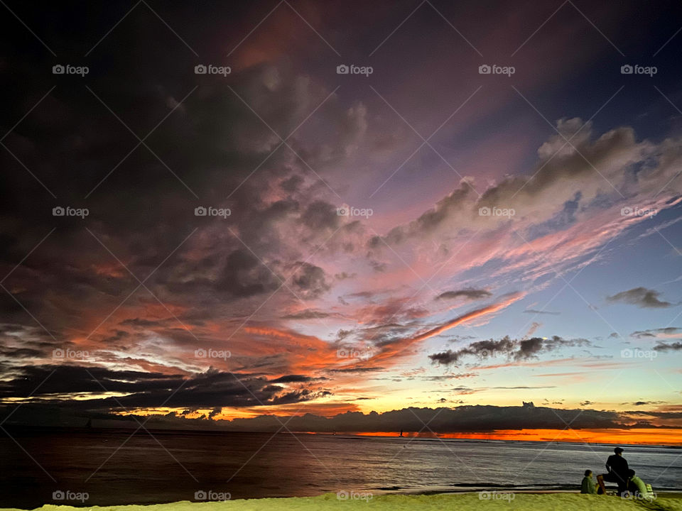 Three figures watching a sunset from a strip of beach