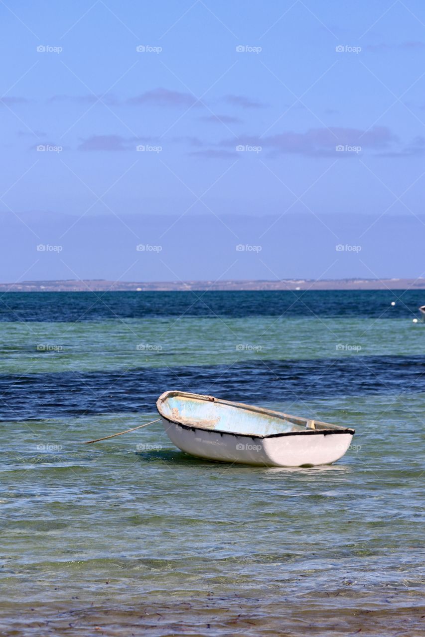 Old weathered fibreglass rowboat on anchor in ocean 
