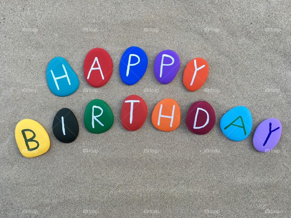 Happy Birthday on colored stone letters with sand background