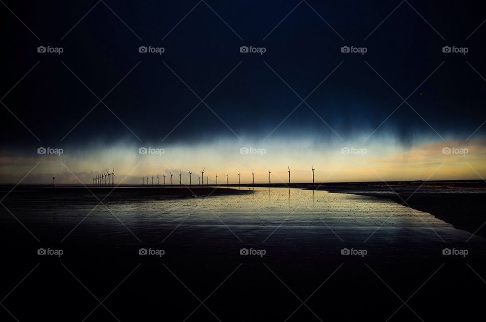 A coastal wind farm is lit by shafts of sunlight breaking through
