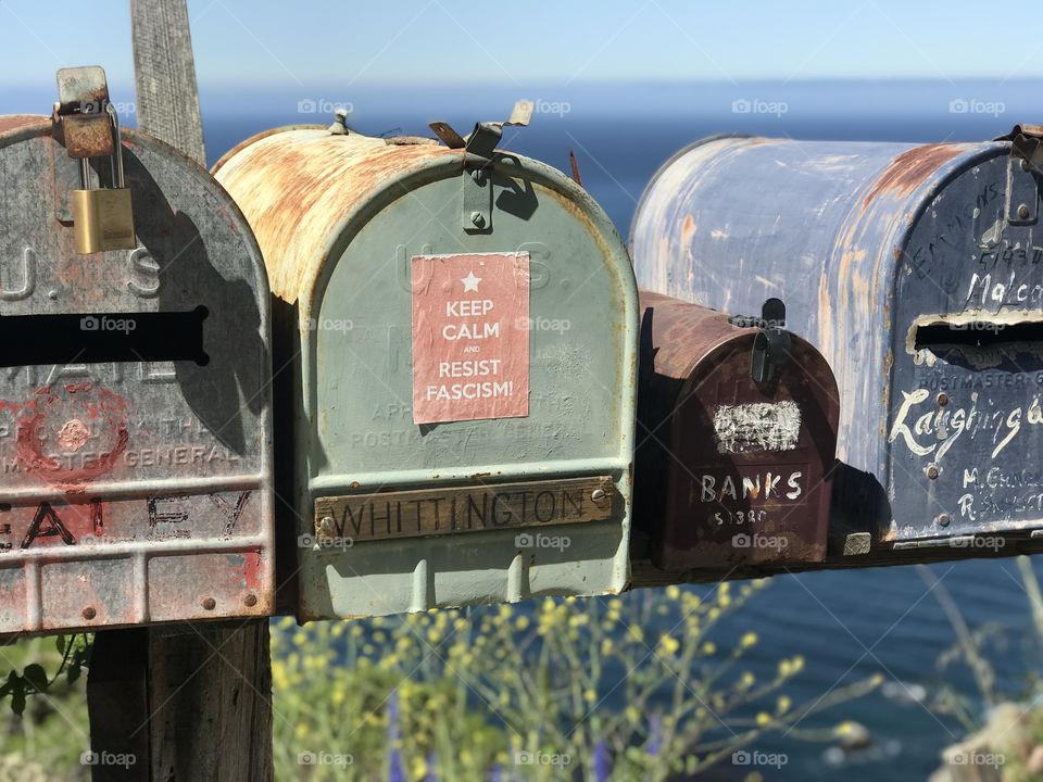 Weathered mailboxes aligned along a winding road, with a background of the pacific. 