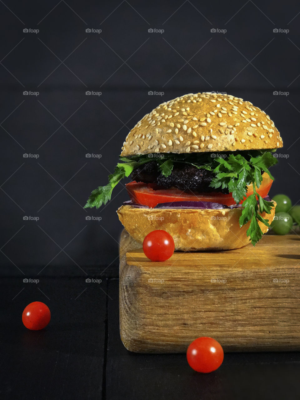 delicious hamburger with bun, served on the board with a small red cherry tomatoes