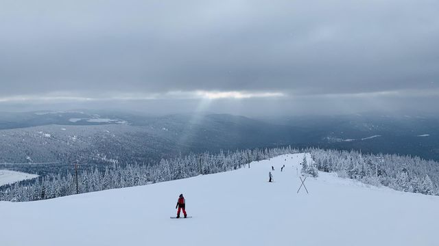 The outgoing ray of the sun shines through the clouds on the ski slope