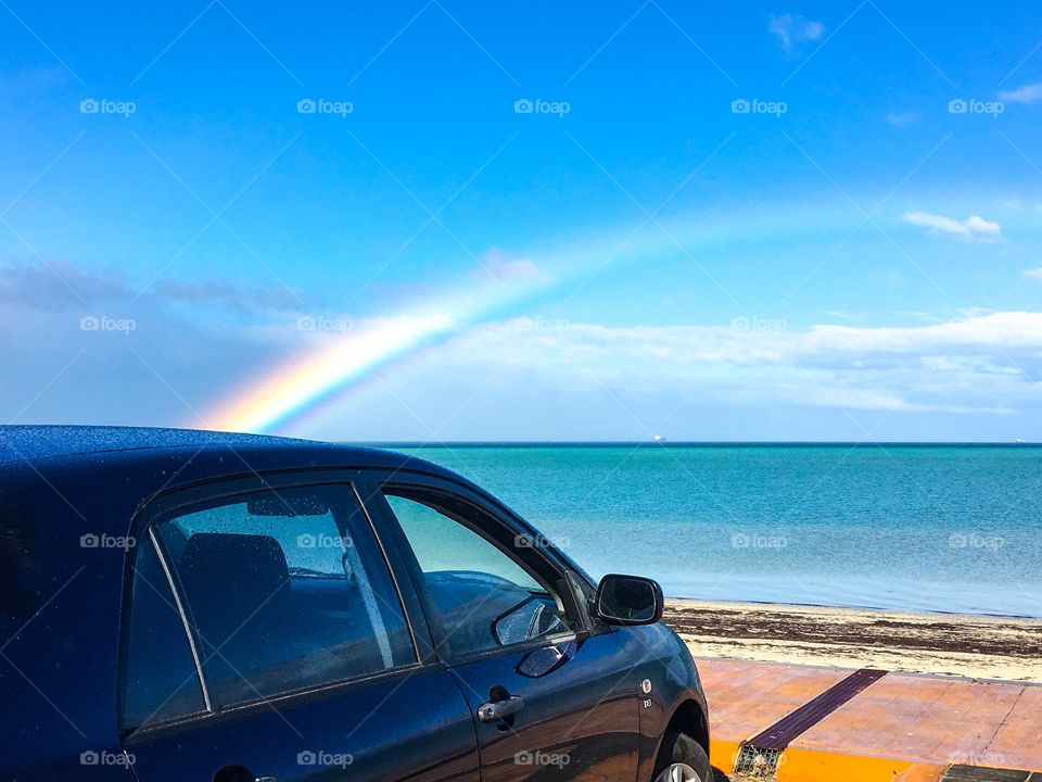 Bright rainbow over ocean blue car in foreground