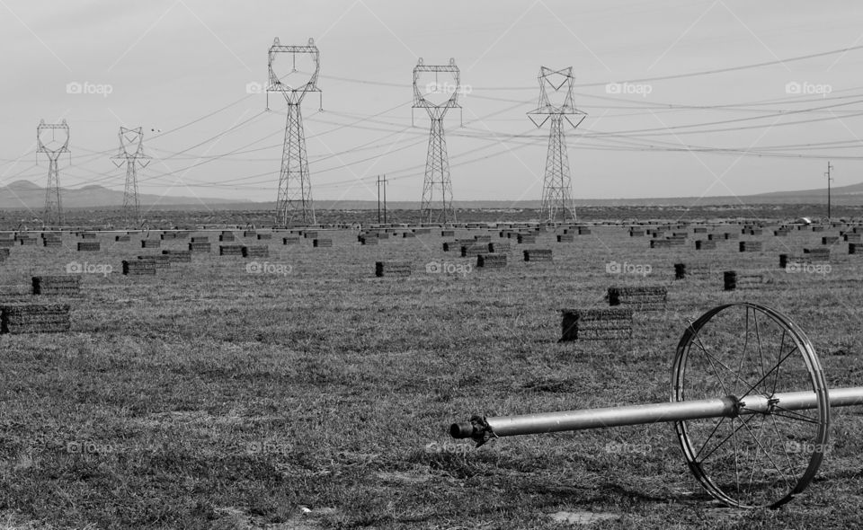 Giant electricity towers running through a field with freshly cut hay bales and irrigation pipes in Eastern Oregon on a sunny fall day. 