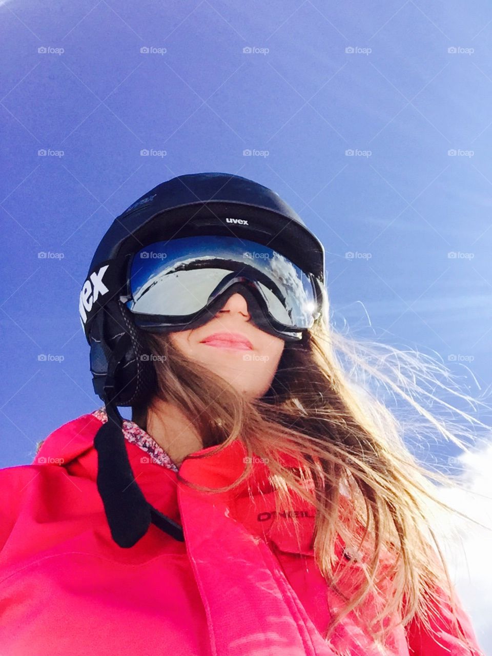 Portrait of woman wearing Uvex ski helmet and Uvex ski glasses with snow reflecting in the ski glasses and with blue sky above