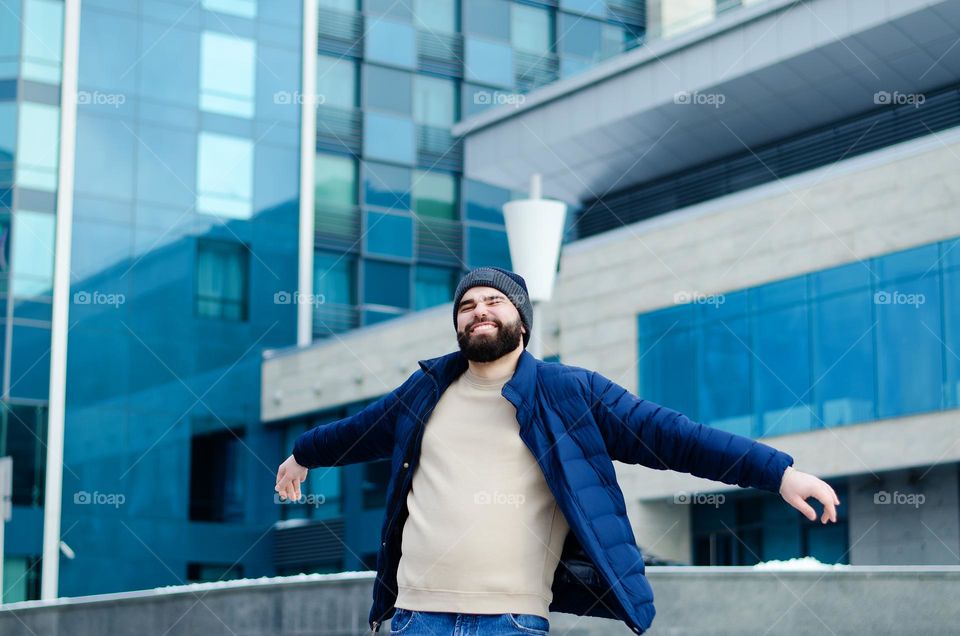 Portrait of happy, smiling, friendly bearded young man in casual clothes walking in city street in winter. Ukraine