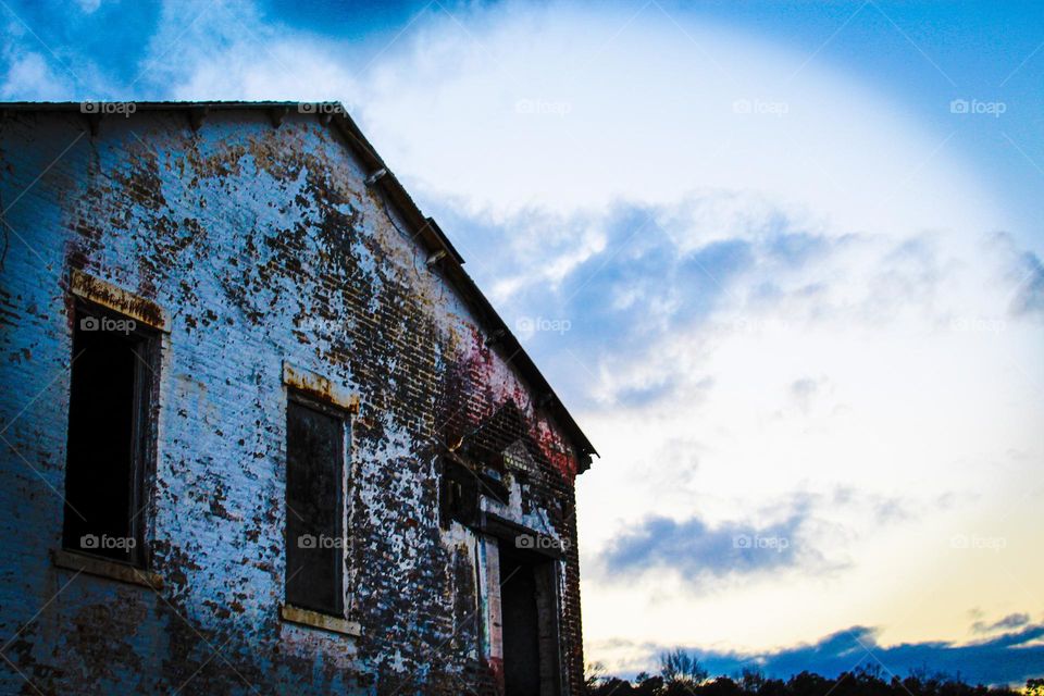 As the sun sets, a small abandoned building creates a stark contrast with the fading sun