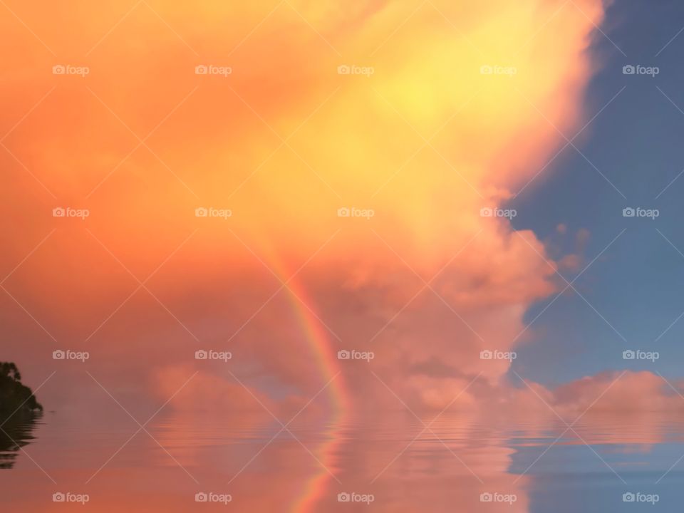 Beautiful rainbow bursting from an Orange cloud and reflecting into the water.