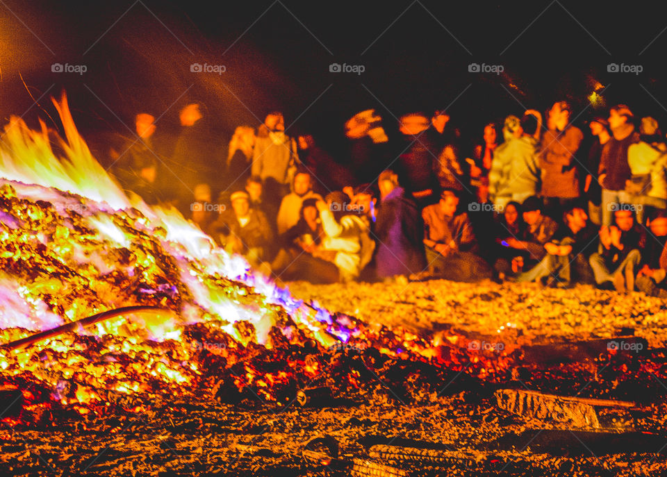 Groups of people sit around the smouldering remains of Hastings Bonfire, on the pebbled beach