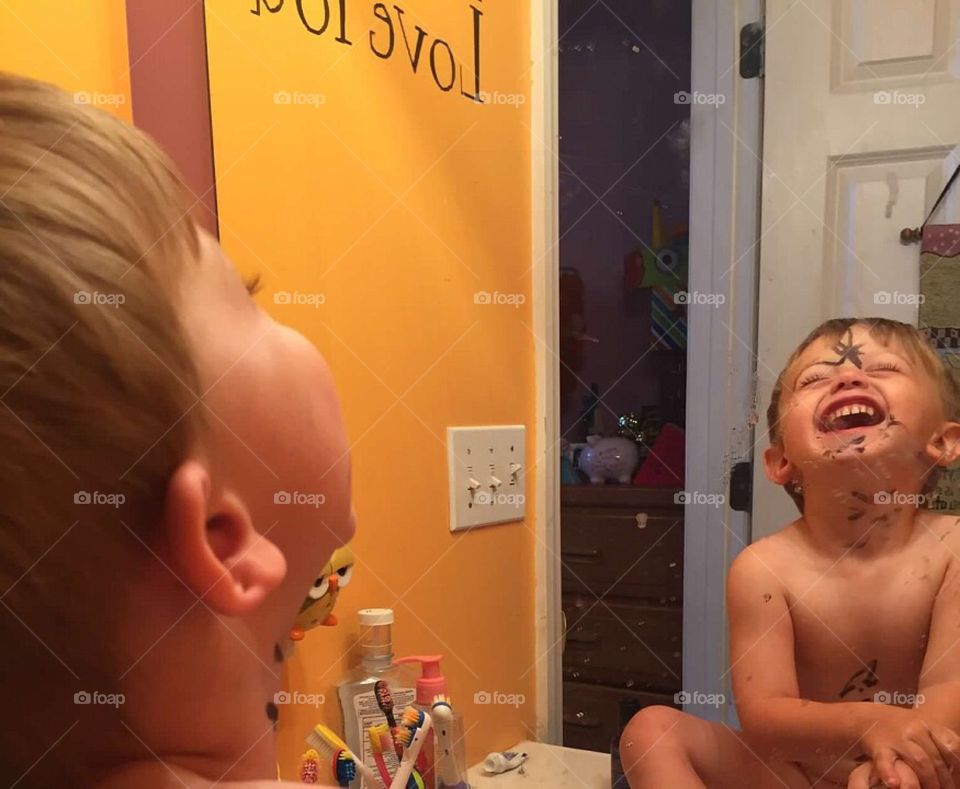 Toddler boy laughing at the drawings he put all over his face. 