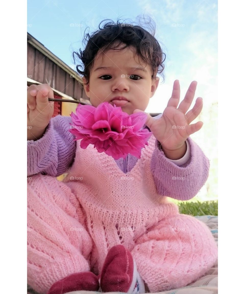 Bebê com uma flor nas mãos.