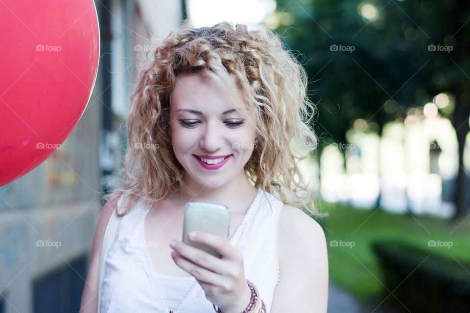 cute curly girl typing on the phone. curly blond cute girl with big red ballon typing on the phone