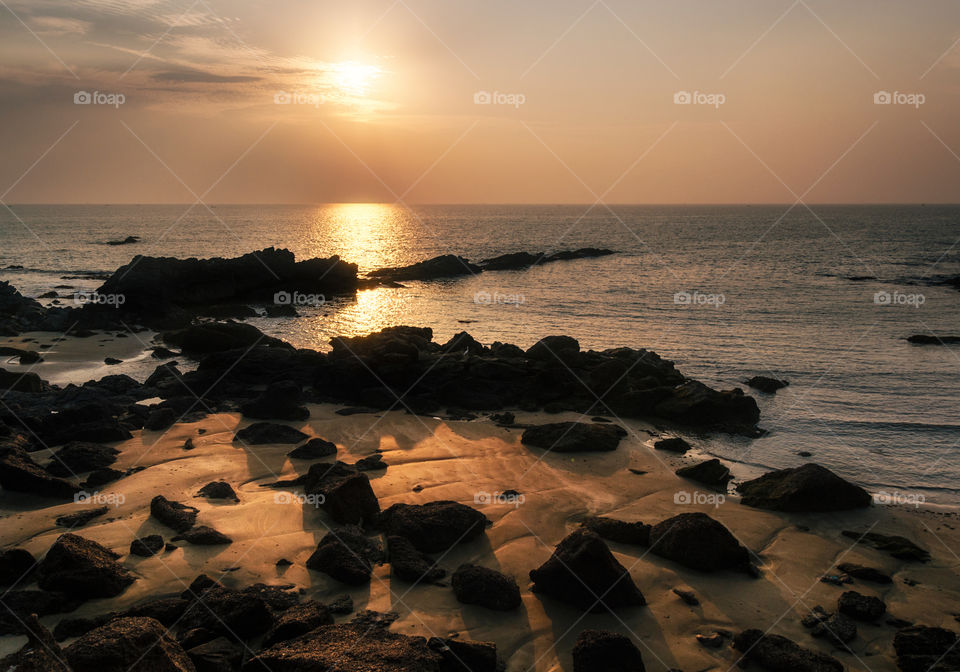 Wild beach with cliffs and rocks at sunset, Goa, India