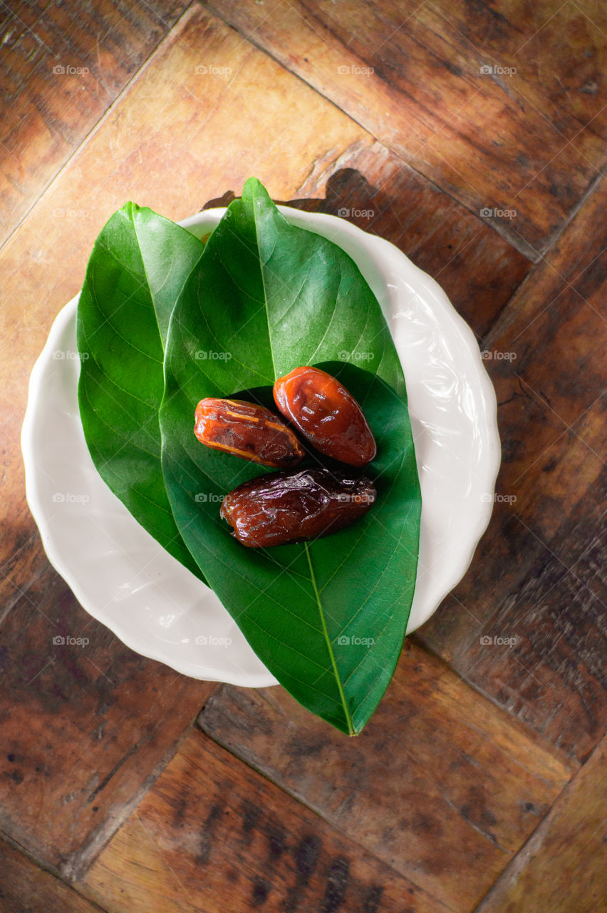Three dates in a white plate with a leaf on a wooden table
