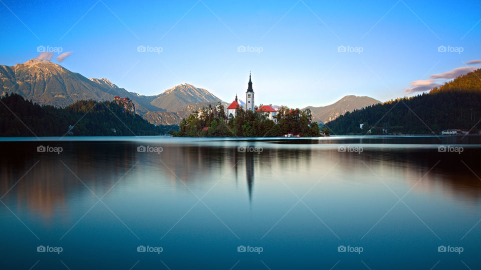 Bled in Blue. The enchanting Lake Bled with its island and the castle above the rock illuminated by the last rays of sun at the end of a late summer day.