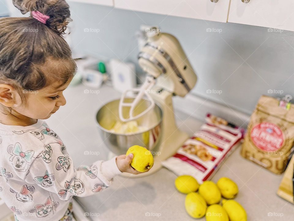 Little girl helps mommy in the kitchen, toddler girl picks out ripe lemons, making lemon desserts with a toddler, homemade lemon cream cheese bars with powdered sugar, delicious recipes made from scratch
