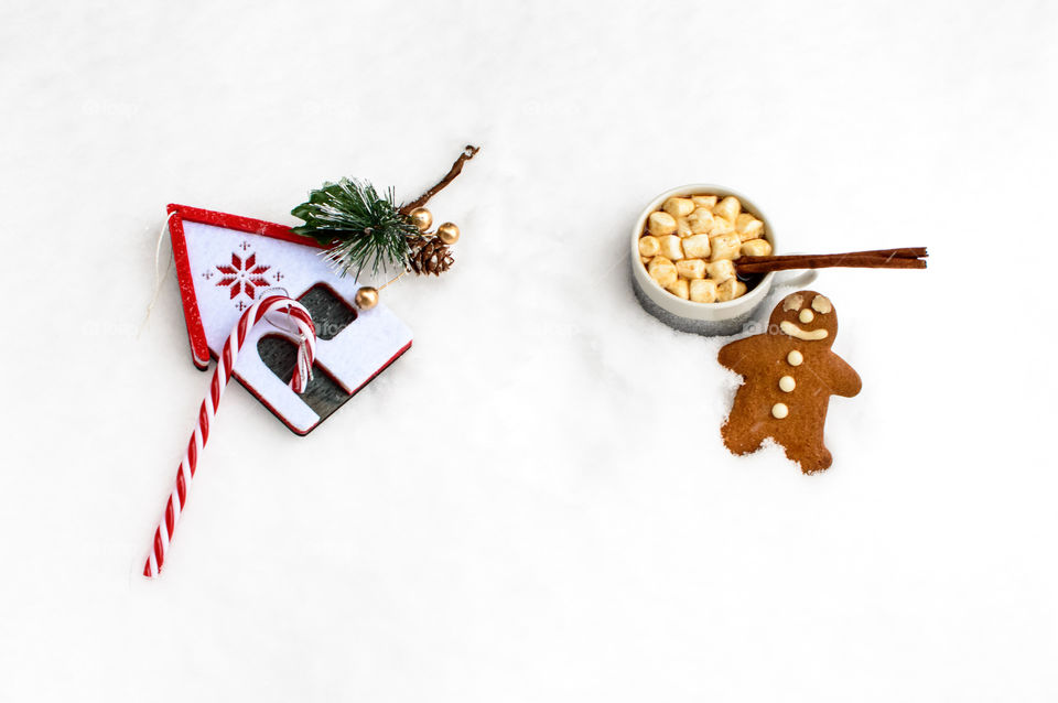 Holiday Christmas vintage gingerbread cookie on fresh snow with hot chocolate with marshmallows next to candy cane ornament traditional Christmas joy and comfort treats on falling snow background with room for copy space  