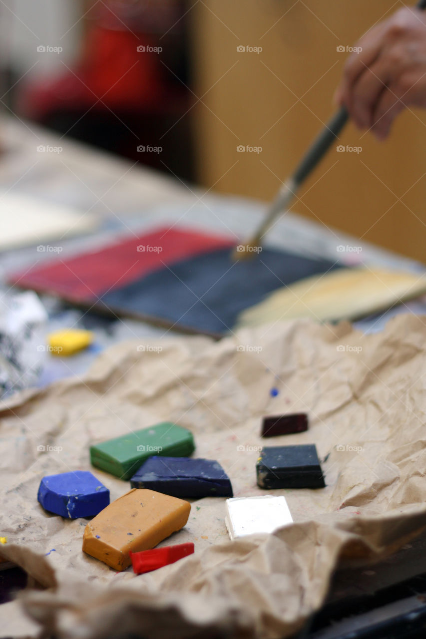 Colorful encaustic paint blocks in the foreground while an artist paints in the background