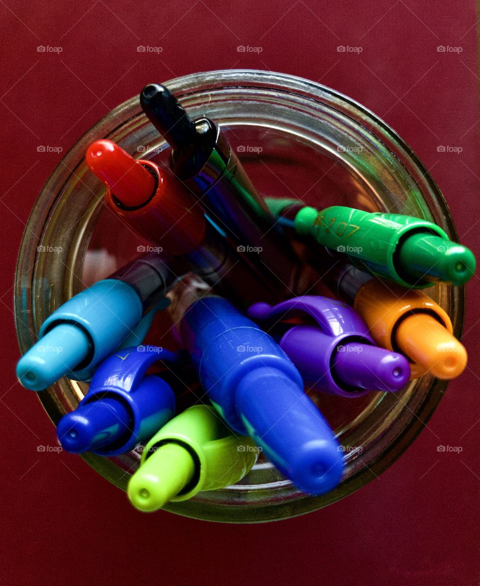Overhead closeup of mason jar filled with colored pens on red background 