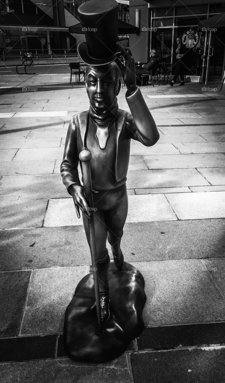 Black and white image of metal statue of a gentleman with top hat in front of shoe