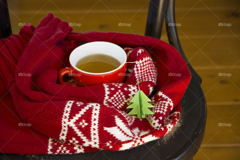 red tea cup and green herringbone tea label on chair wrapped in warm red sweater, cold season, warm clothes, hot drink