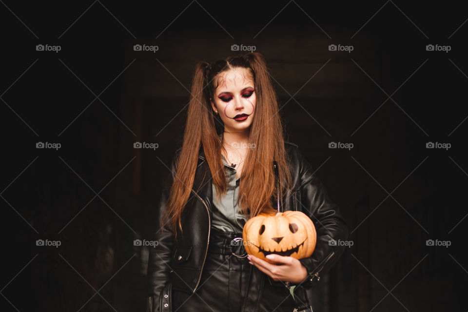 Young Woman holds a pumpkin in her hands. Painted pumpkin. Woman with bright makeup for Halloween. Halloween 2020. Place for inscription.