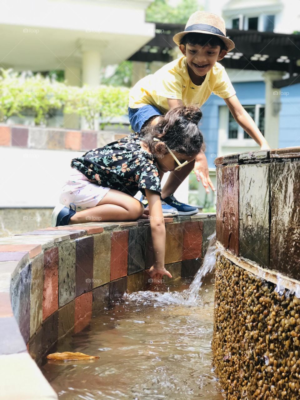 Both brother and sister playing at fountain in fully summer outfits.