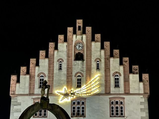 Illuminated Christmas star on the town hall in Hammelburg by night with the figure from a fountain in front of it.