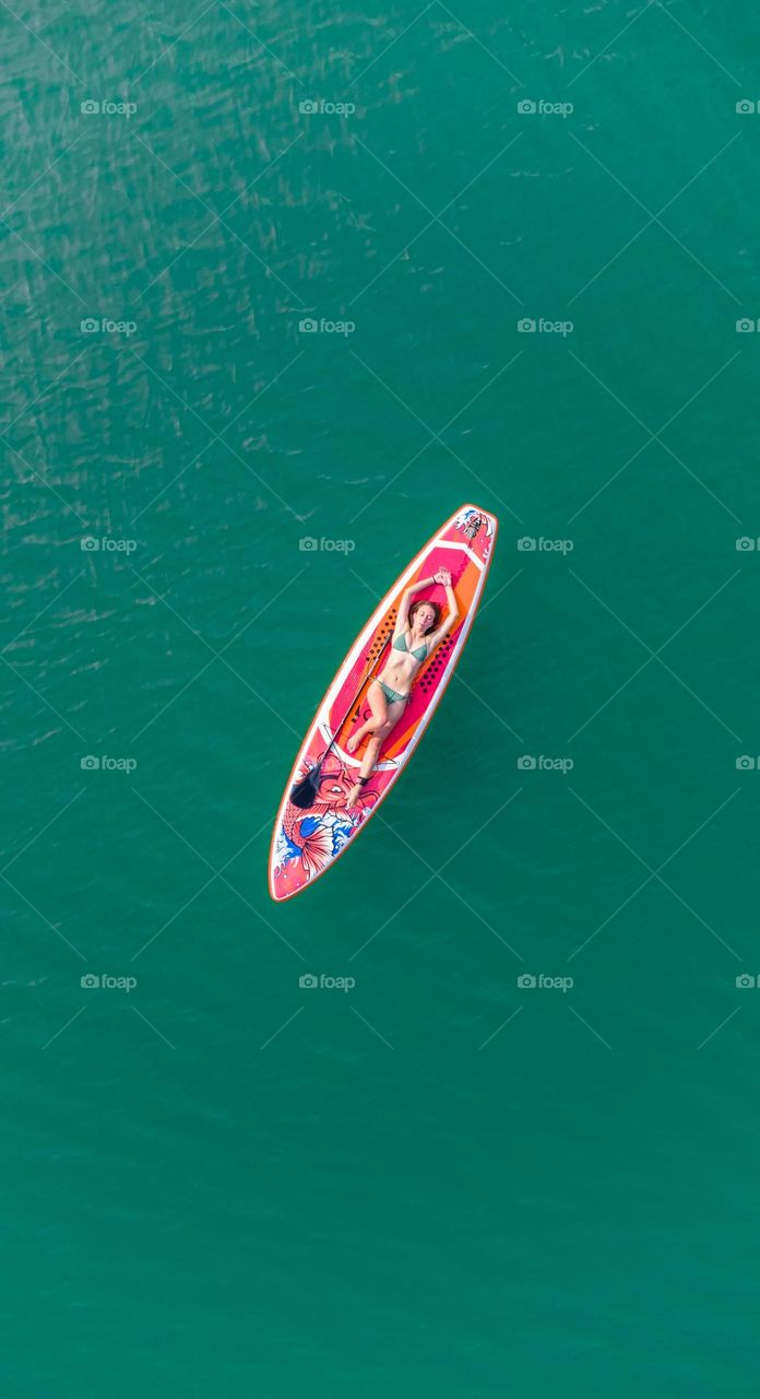 Young woman enjoying the sun in the summer, laying on the sup board in the middle of the lake 