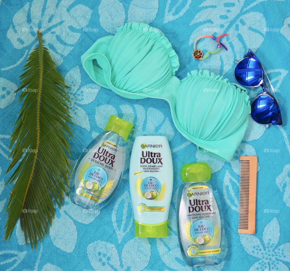 Garnier eau de coco shampoo, conditioner and bath gel on a blue towel with comb and palm leaf and blue sunglasses and bikini.