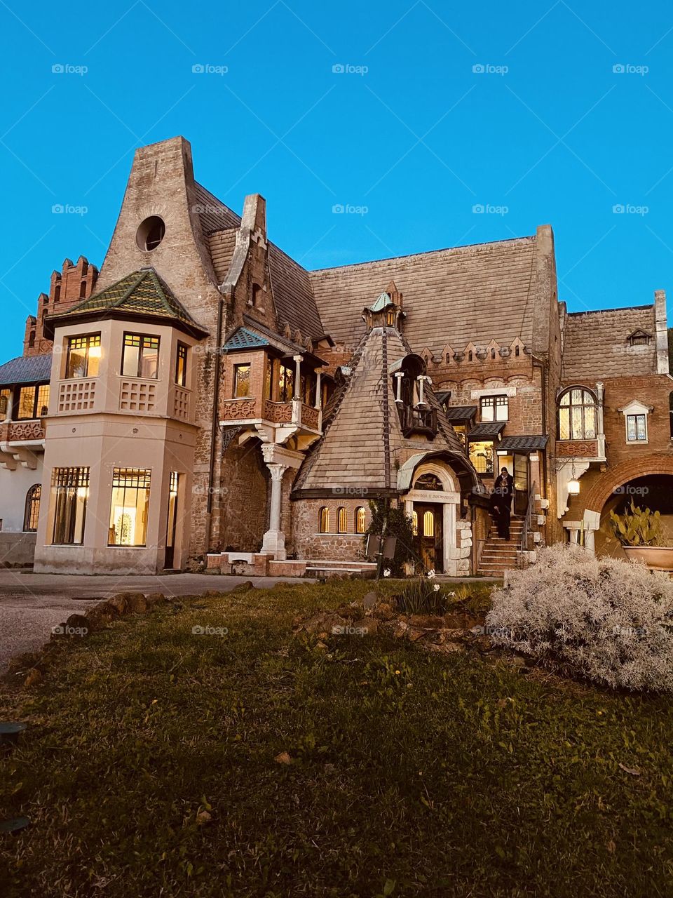 A cozy house stands in the evening quiet, its windows glowing with warm golden light. The soft illumination contrasts with the surrounding darkness, creating an inviting and peaceful atmosphere.