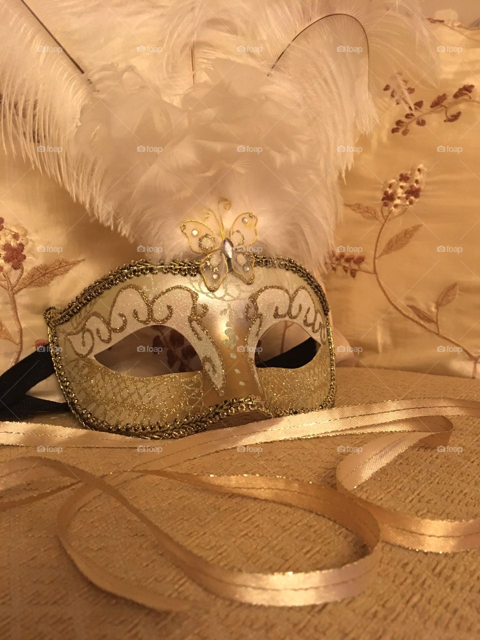 Gold Venetian masquerade mask with white feathers and gold ribbon in the foreground 