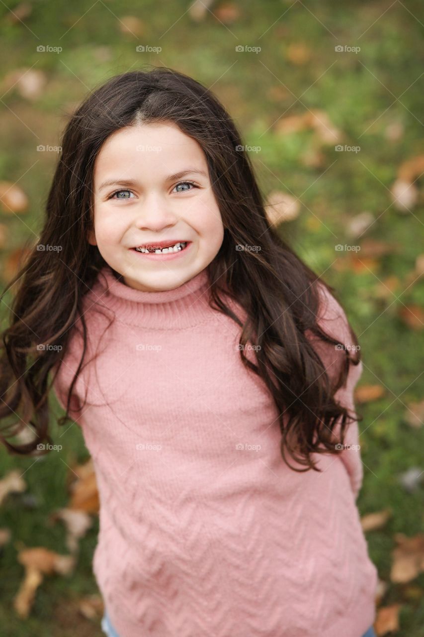 Little girl in pink sweater smiling outdoors with long brown hair