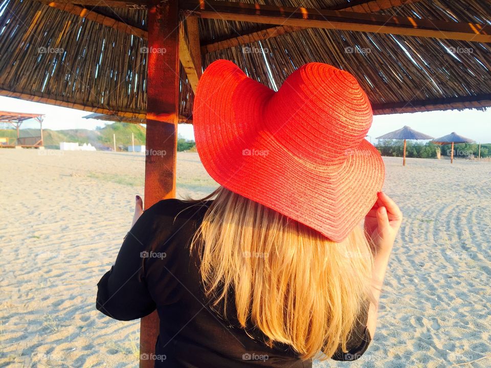 Back of woman with long blonde hair and red summer hat on the beach