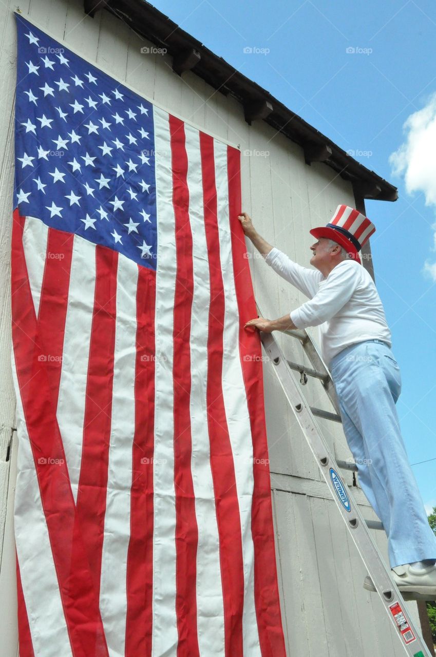 Man wearing Uncle SAMs Hat hangs huge American flag  