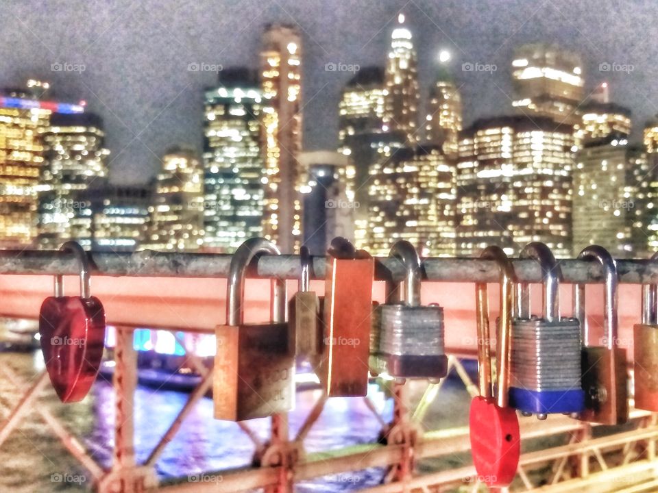 love locks hang from Brooklyn bridge with view of lower Manhattan skyline at night