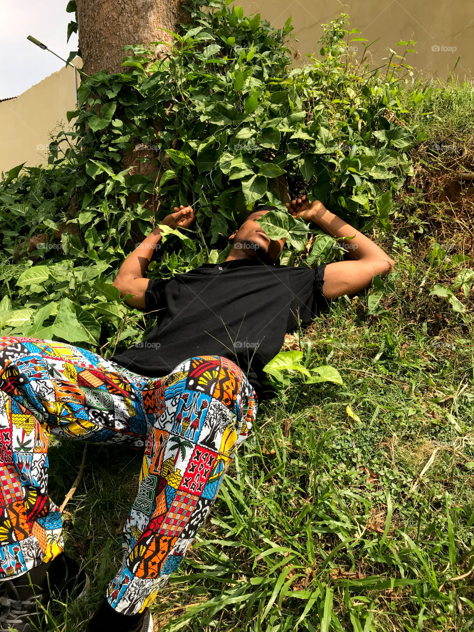 Man in colorful pants resting on grass in a garden 