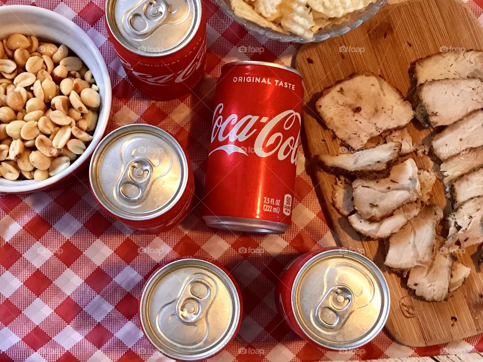 Cans of Coca-Cola on a red and white checkered background with barbecue food and potato chips 
