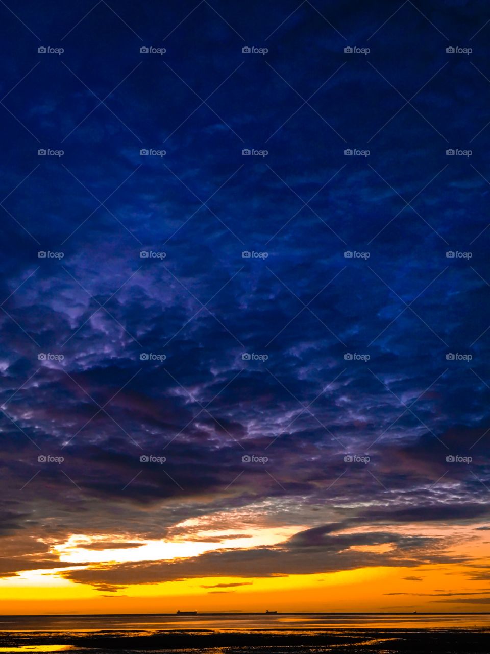 Storm clouds over the ocean at sunrise, ships in distance on horizon 