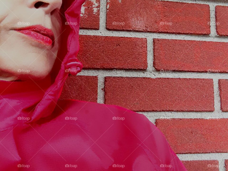 Woman In red leaning against a red brick wall.