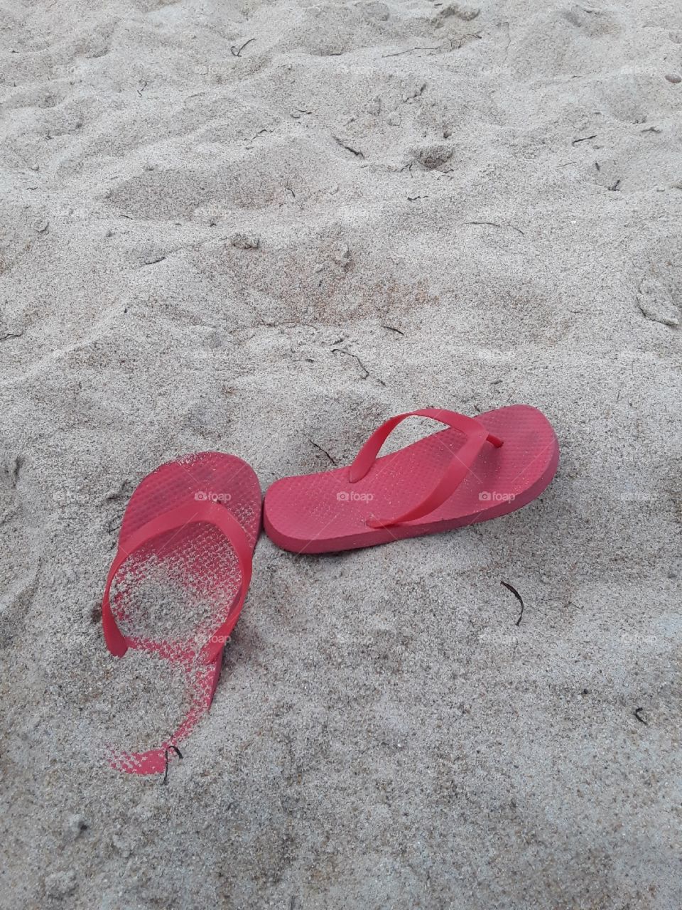 Red flip-flops partly buried in the sand. Taken at Virginia Beach, Virginia.