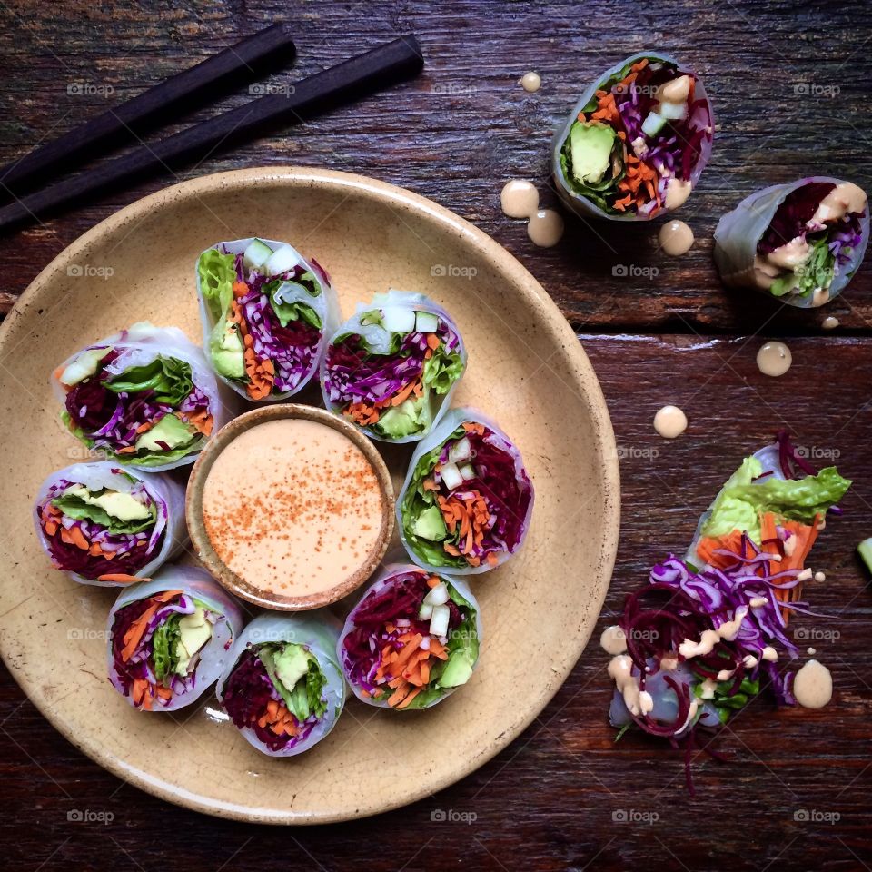 Colorful Vietnamese summer rolls with dipping sauce on a plate with chopsticks.