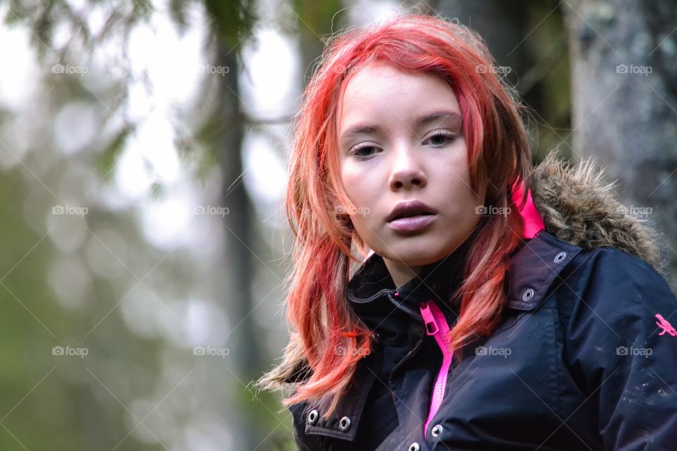 Girl with a serious look in the face sitting in the forest with warm outdoor clothing