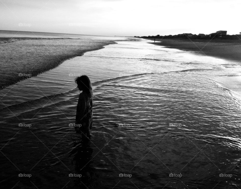 Black and white image of the silhouette of a little girl on the beach pondering the vastness of the ocean at Emerald Isle North Carolina 